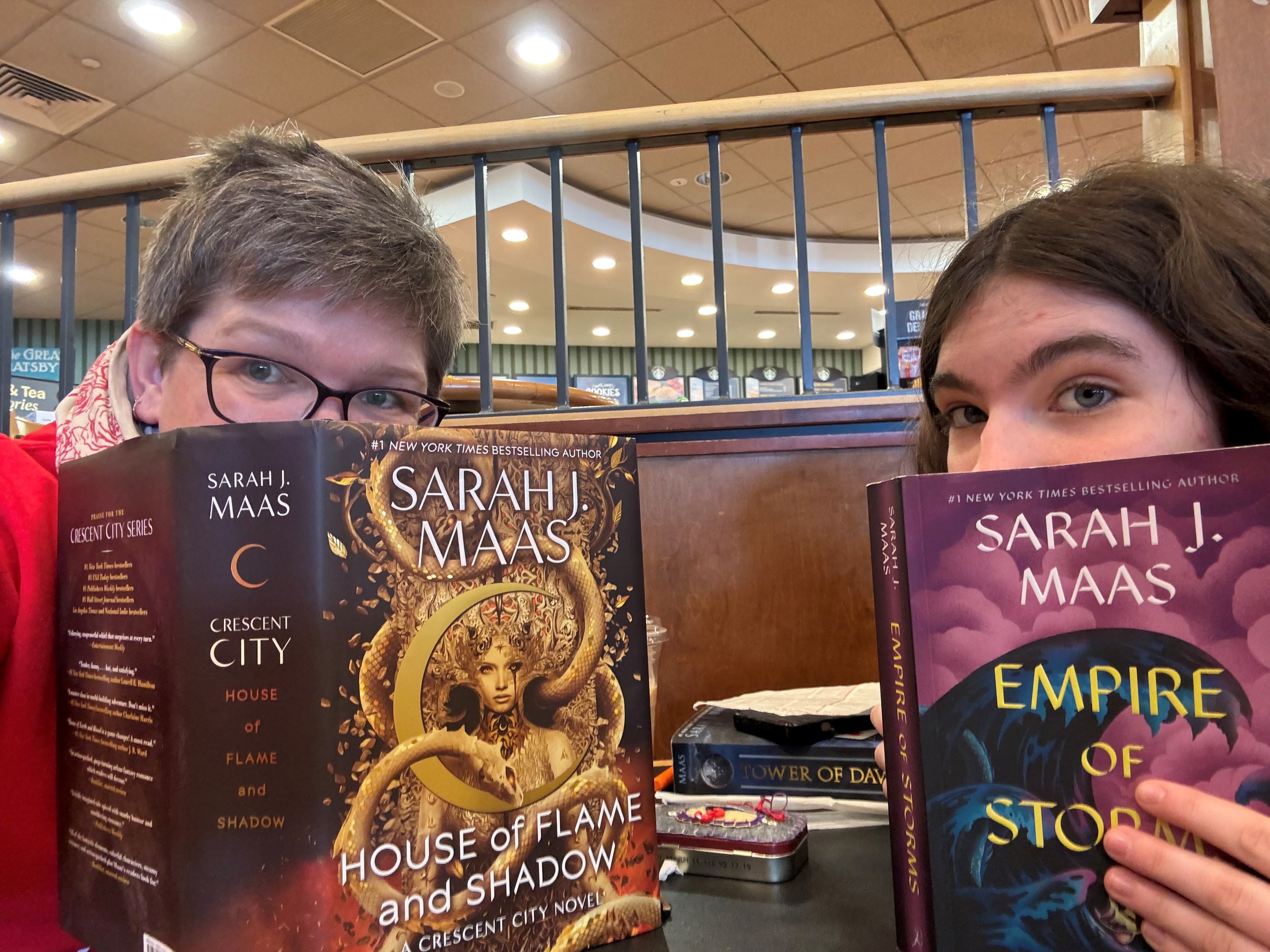 Kara peeks over the edge of House of Flame and Shadow, and her daughter peeks over the edge of Empire of Storms. Both books are by Sarah J. Maas.