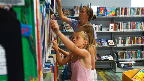 A woman and two young girls browse the shelves of a rural library branch.