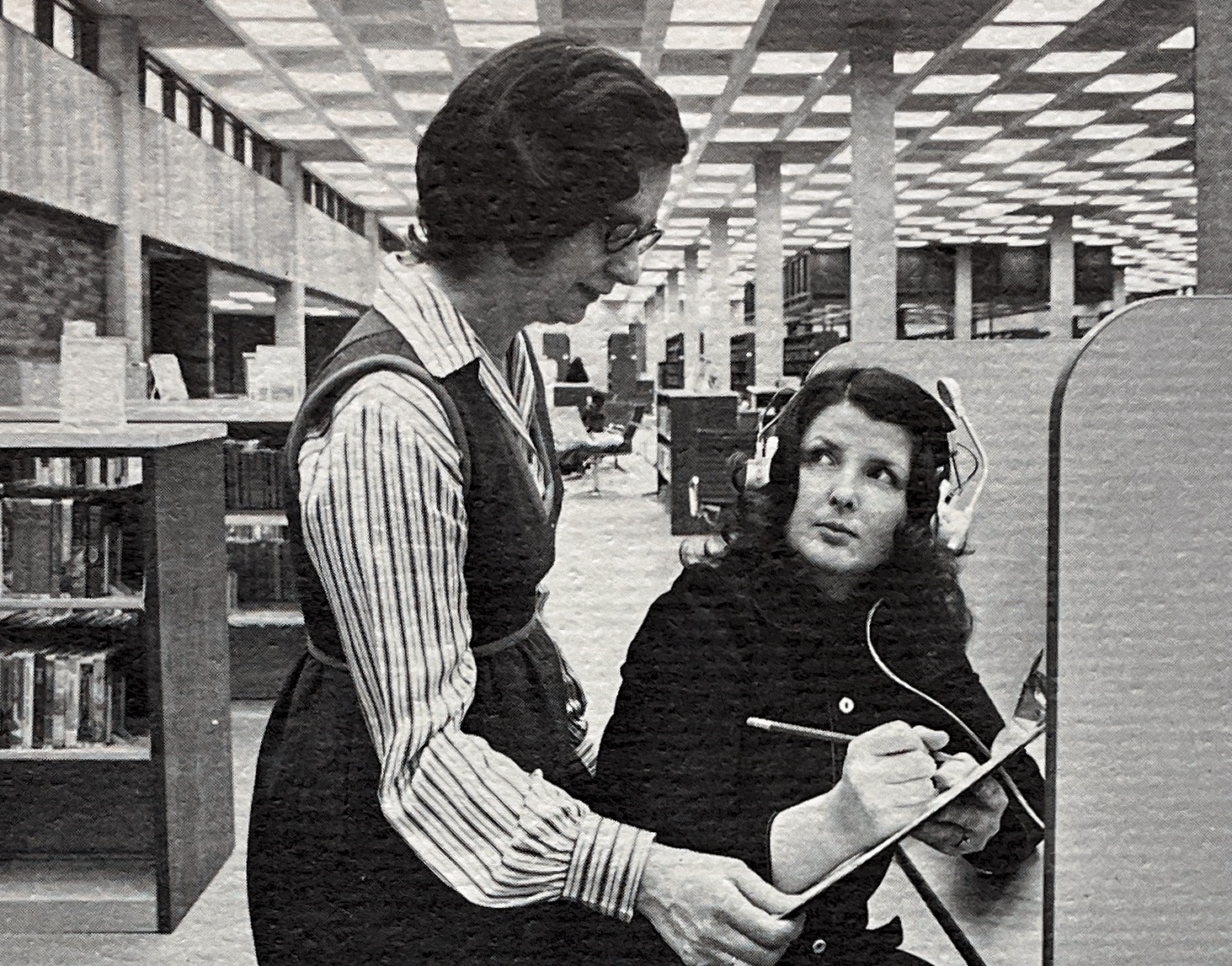 A librarian in 1970s-era style assists a customer inside the Main or Downtown Library