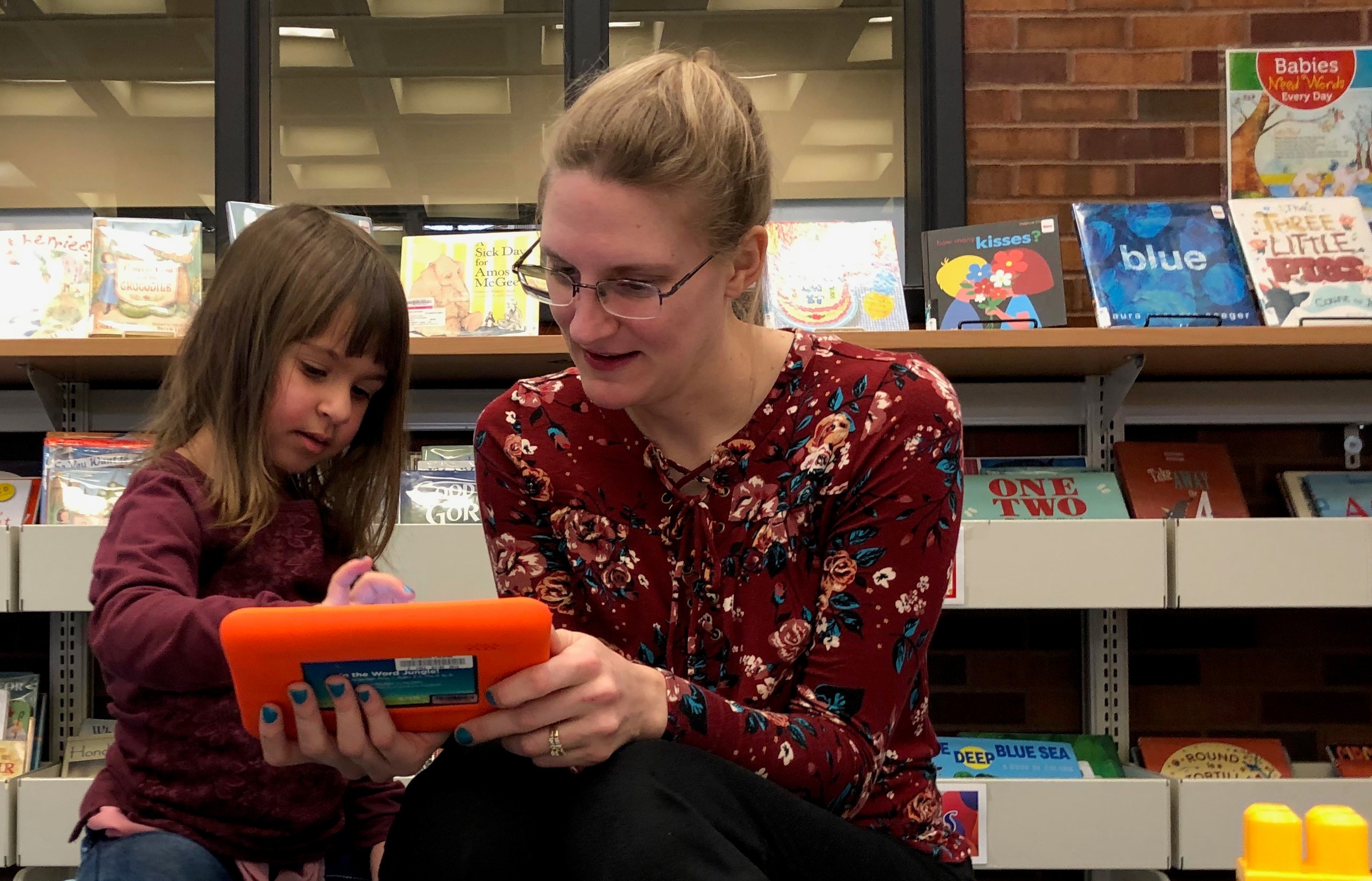 A mom and her daughter play on a library learning tablet.