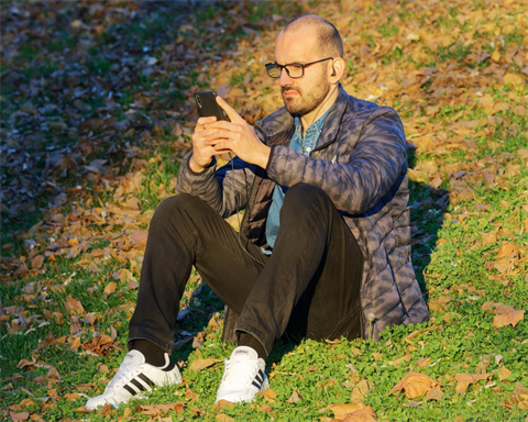 A man sits on a hill, looking at a smartphone.