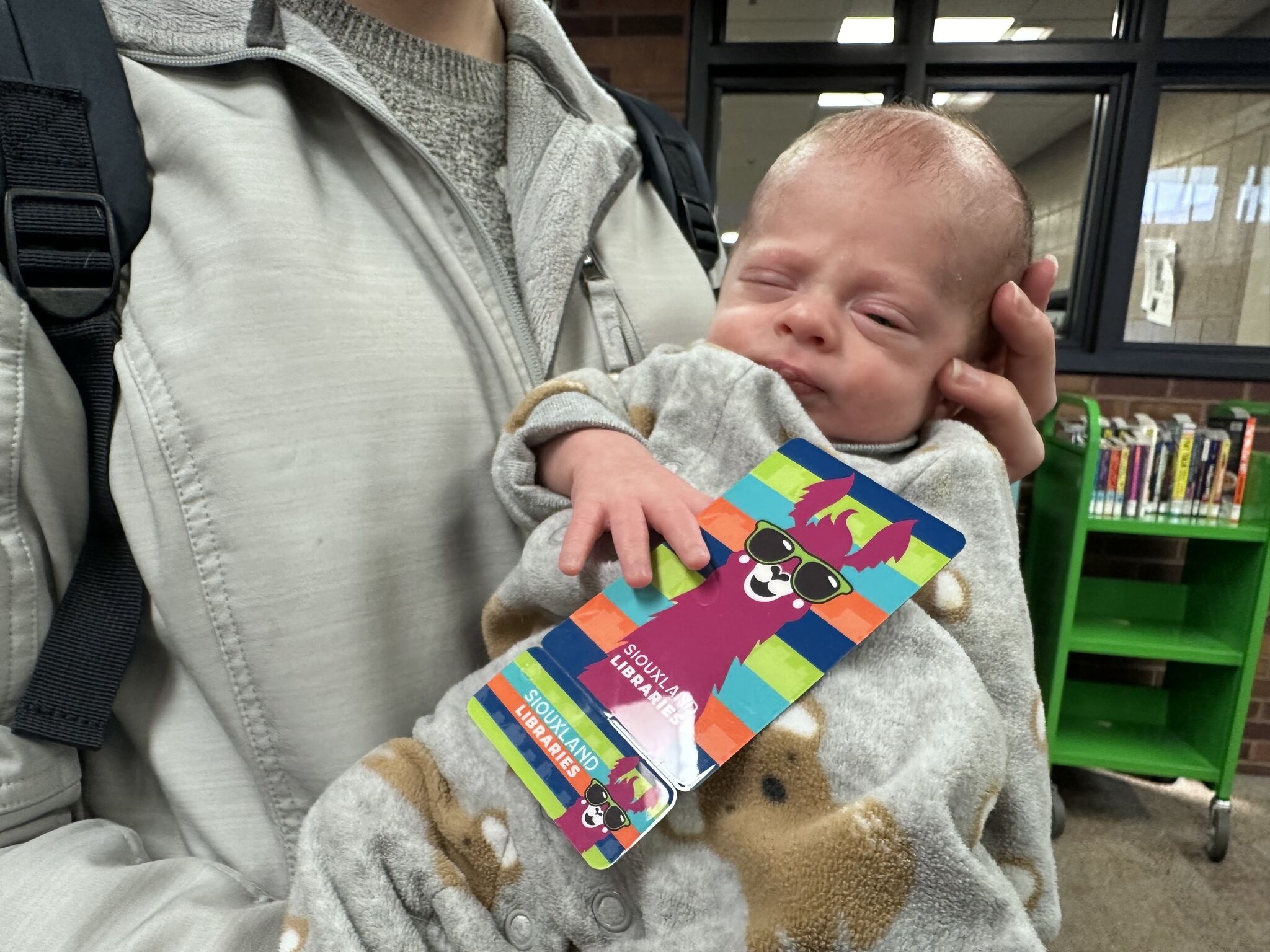 A sleepy infant holds the llama library card between his fingers.