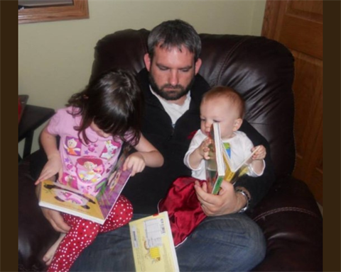 A dad sits and reads with his two small children.