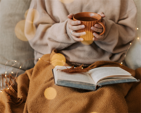 person reading with a blanket and a mug